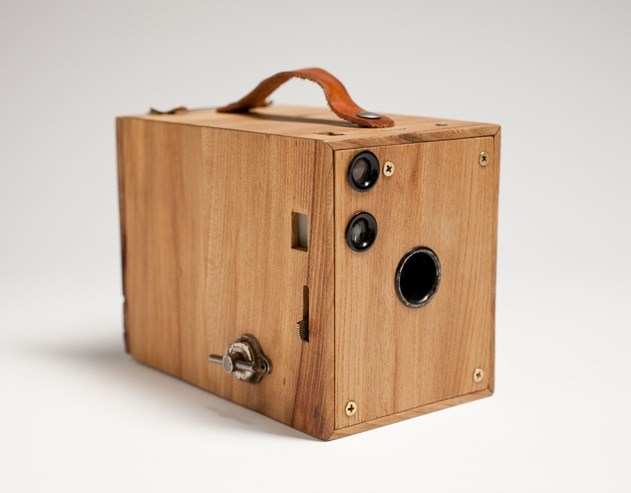 Wooden box with handle on top, three lenses on one side and something to adjust on the other