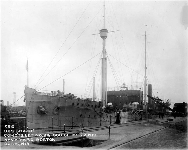 Black and white image of a large board with two masts at a dock