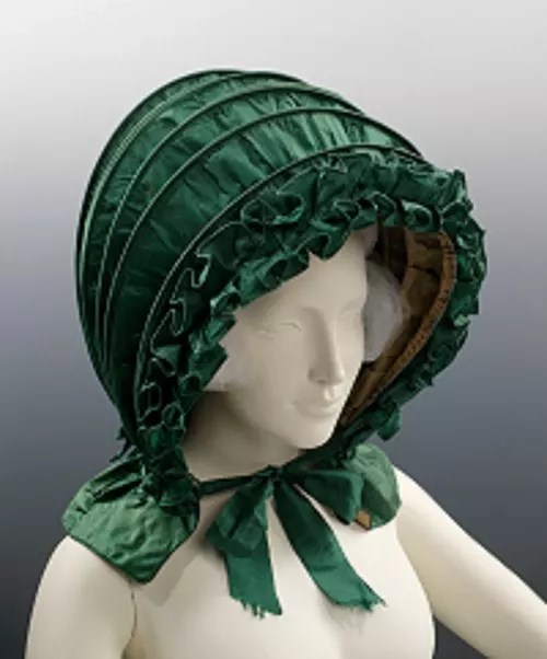 A green calash headpiece worn by a mannequin