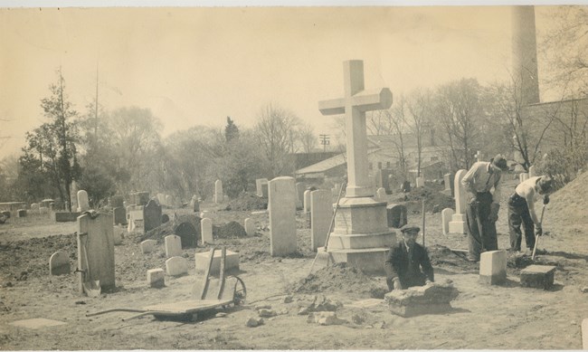 men working, with shovels, in a cemetery, many gravestones visible