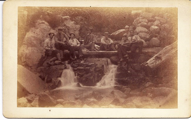 a group of men pose near a waterfall