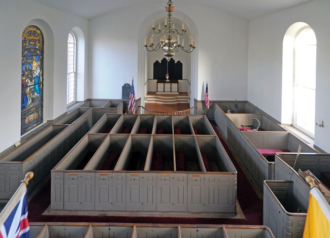 church interior, with tall wall box pews, chandelier & flags visible