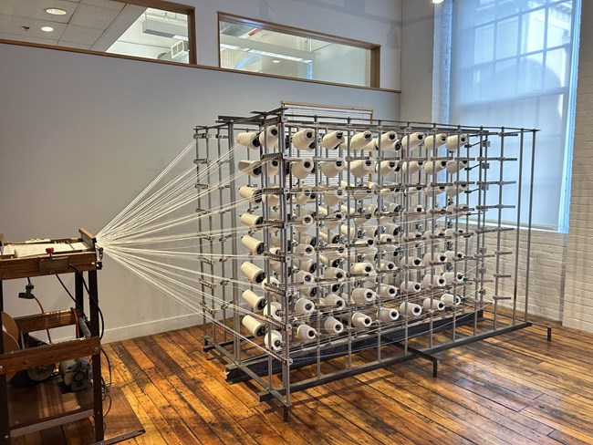 A metal frame full of many rolls of thread. Each roll has a thread that has been pulled forward into a machine.