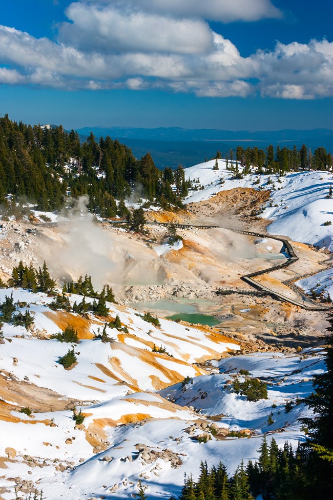 Photo looking down a valley with patches of snow on hydrothermally altered rock and soil.