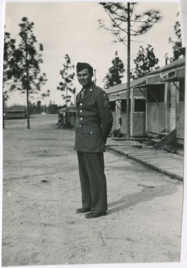 A man in a military uniform standing in front of a barrack.
