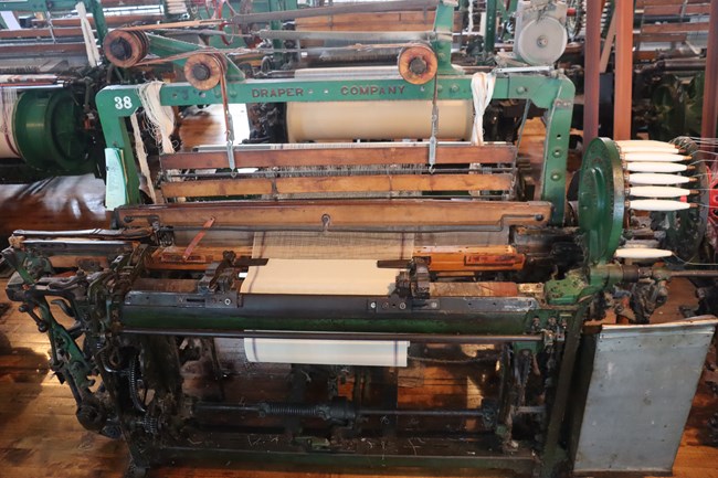 A large machine made of metal and wood. the metal frame is painted green and labeled "Draper Company"