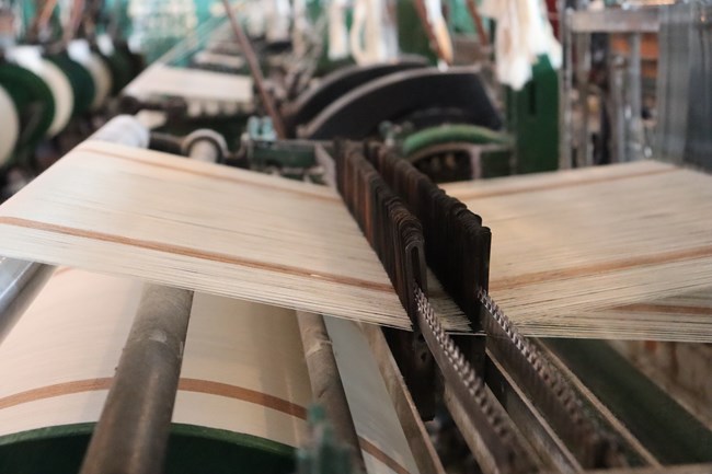 long threads laid out in a line, holding up thin pieces of metal.