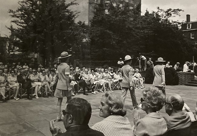 Women model NPS uniforms in front of a seated crowd.