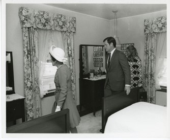 Rose and Ted Kennedy walk by a bed and curtained windows at the JFK Birthplace