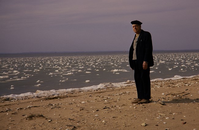 Freeman Tilden stands on a beach at the edge of the water in a suit