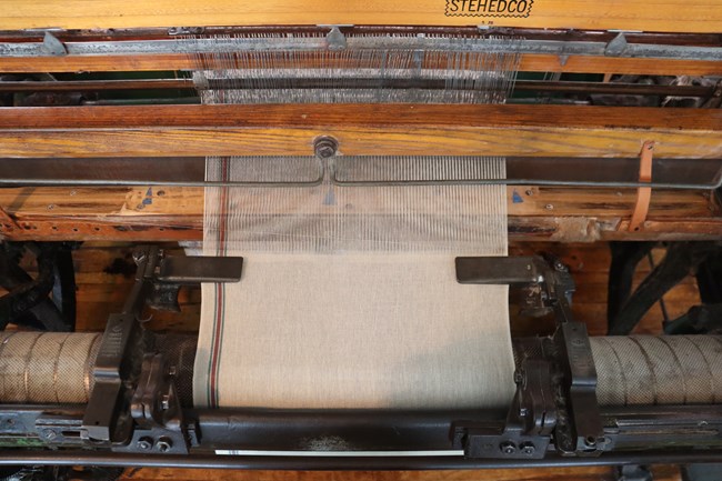 Top down photo of a loom focused on the moment unwoven threads transition into woven material.