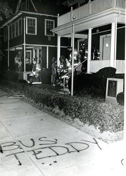 a sidewalk spray painted with the words "Bus Teddy".  The JFK Birthplace sits to the right.