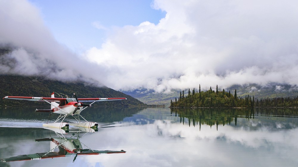 Plane floating on a clear body of water between mountains concealed by fog.