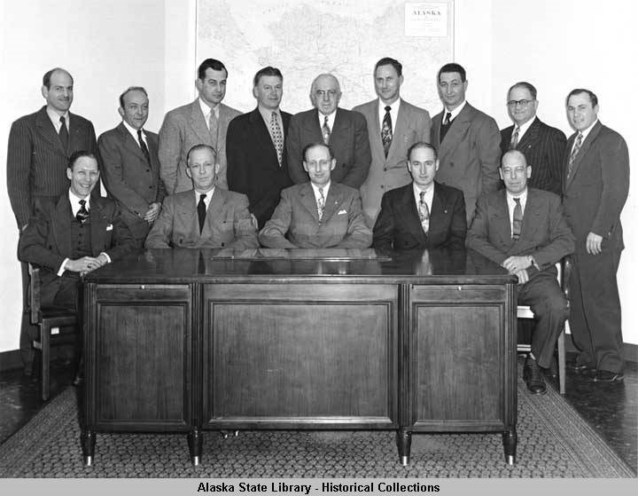 about a dozen men in business suits posing for a photo behind a desk