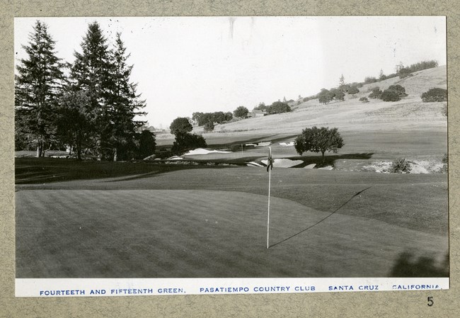 flat area of golf hole with sand traps, trees, and hills in the distance