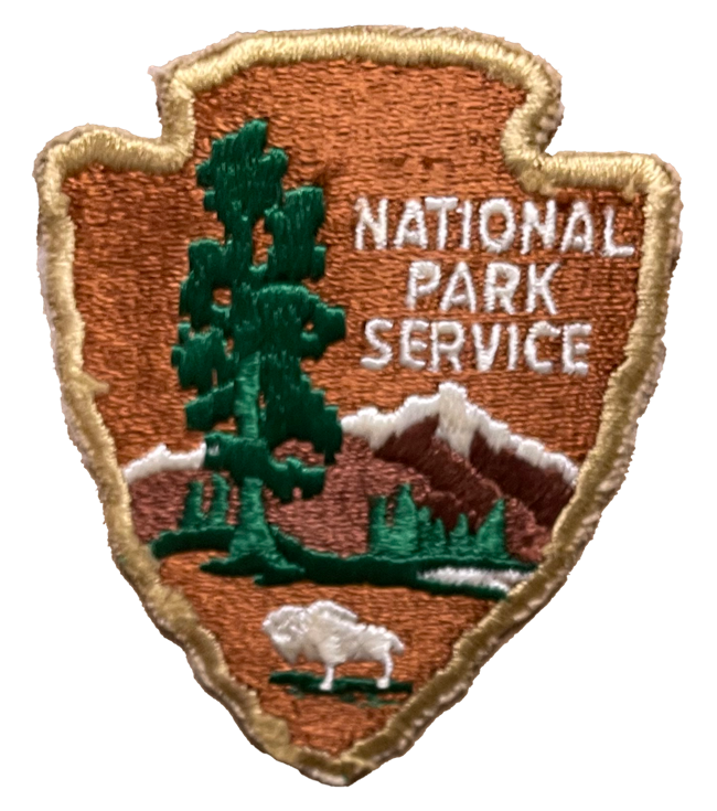 Arrowhead with bison, tree, mountains and words, with gold trim