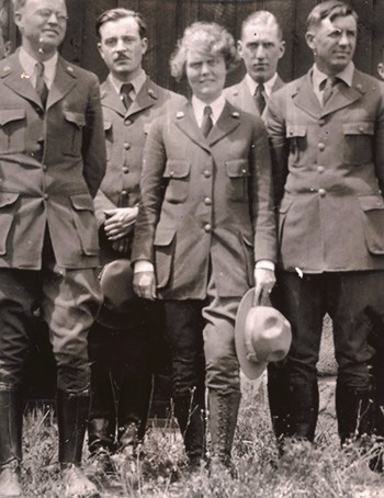 Five uniformed rangers stand facing the camera.  The one woman of the group stands in the middle holding her hat.