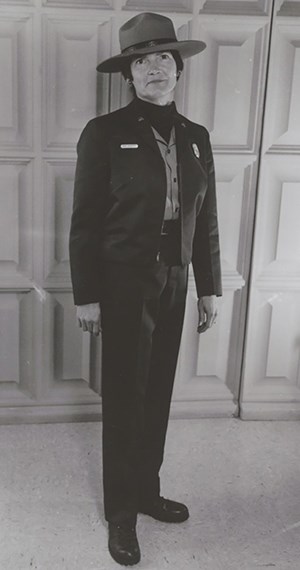 Female ranger seen in traditional dress, a wide brimmed hat, short long sleeve jacket, dark dress slacks and dark oxford style shoes.