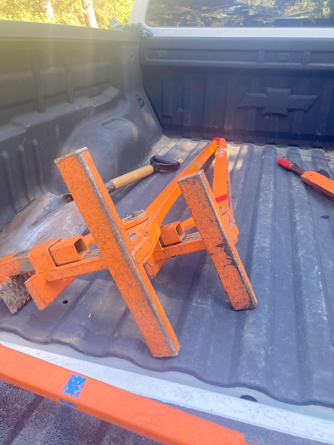 A large, metal lever-like contraption in the back of a pickup truck. It's mostly bright orange, but the paint is scratched and worn in several places.