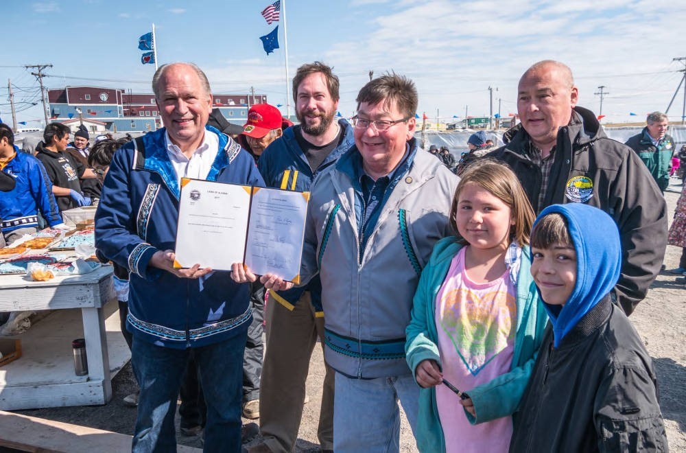 four adults and two children standing outside as one man holds out a paper