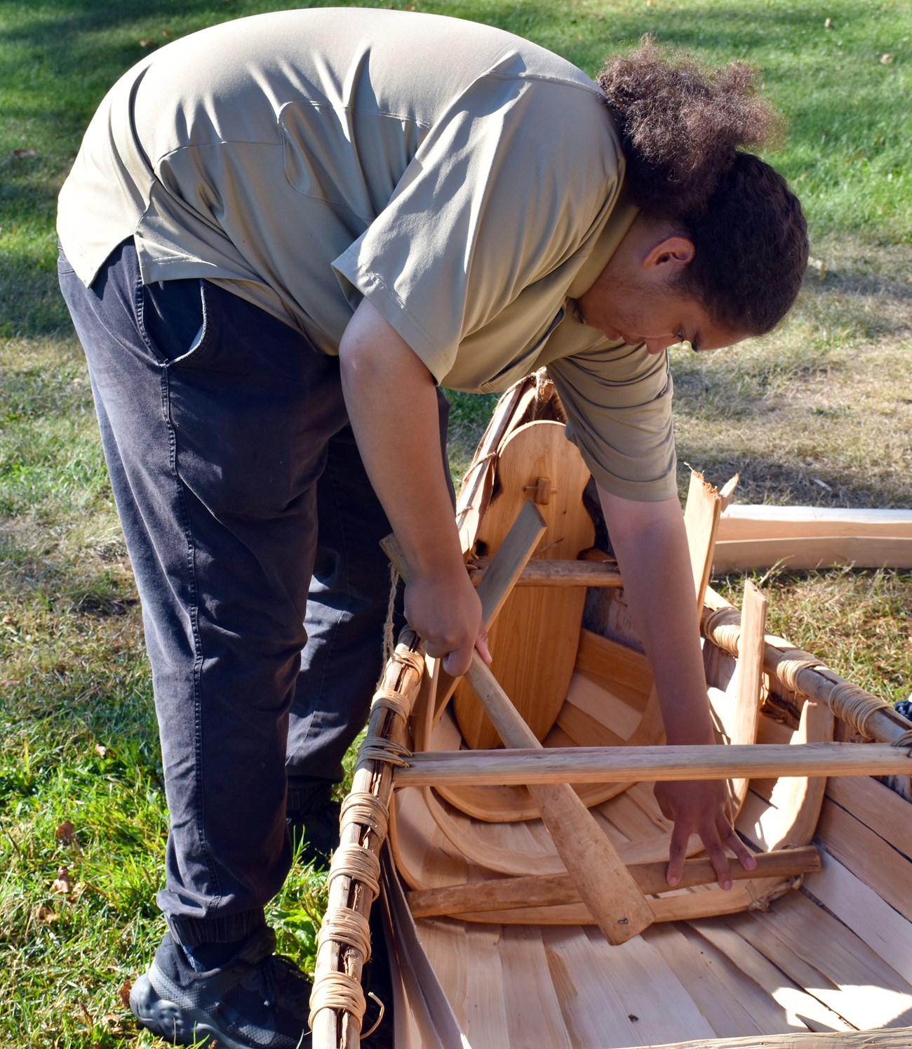 A person uses a wooden tool to hammer a cedar rib into place on the interior of a canoe.