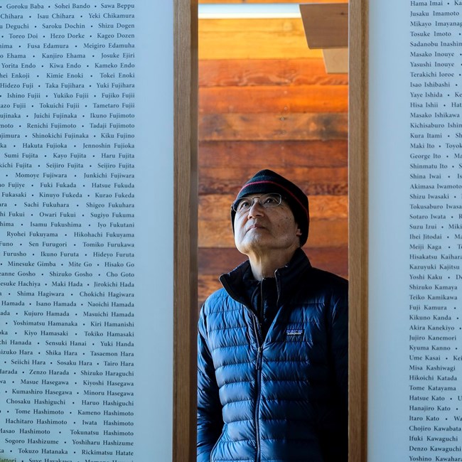 A man looks up at two large panels covered in lists of names.