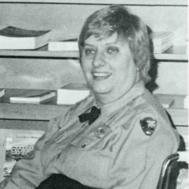 Joann Hodges siting in her wheelchair. She wears a long-sleeved NPS uniform shirt and cross tie.