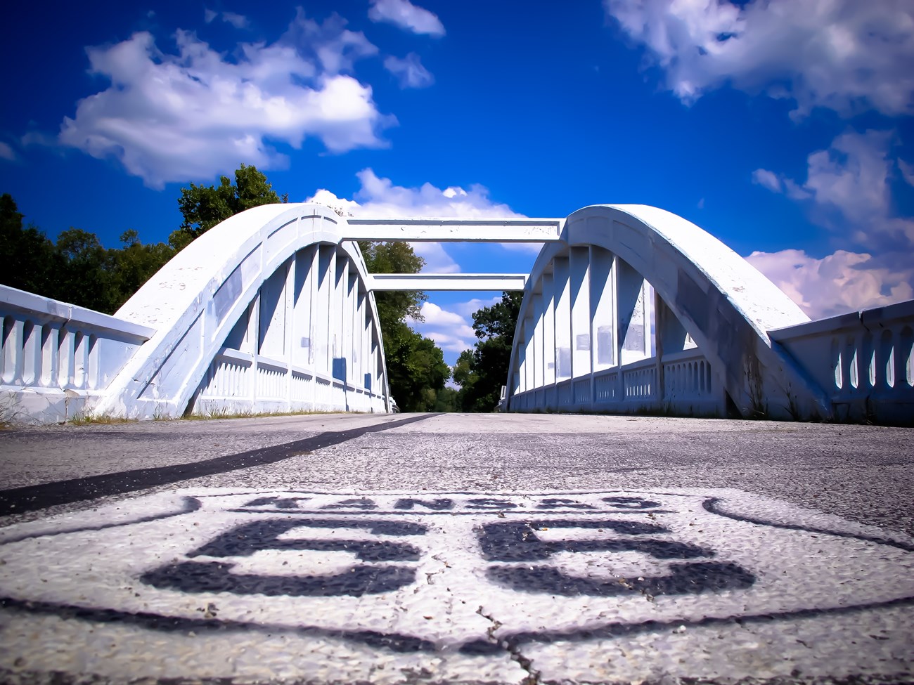 A road with a white emblem that reads "Kansas Route 66" leading up to a white truss bridge.