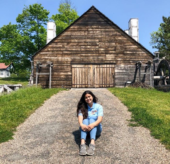 A woman in blue shirt sitting in front of wooden building.
