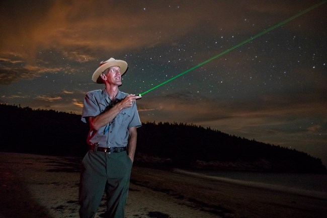 uniformed ranger points a laser pointer across the night sky