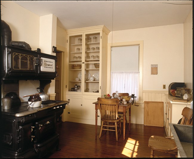 a black stove to the left is flanked by a built in white cabinet with glass doors and a small wooden table with chairs.