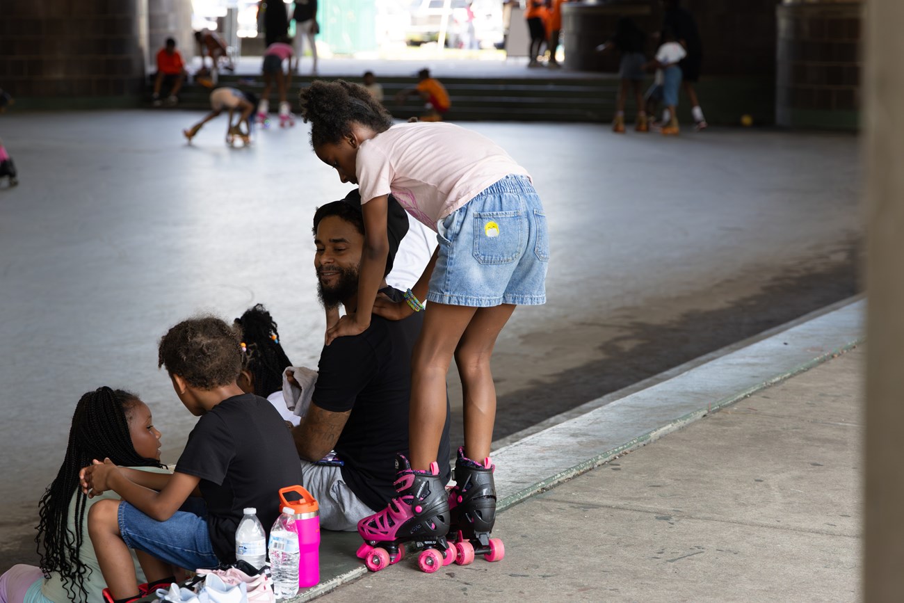 A dad smiles at his four young children as they take a water break on the steps of the rink at Anacostia Park Skating Pavilion