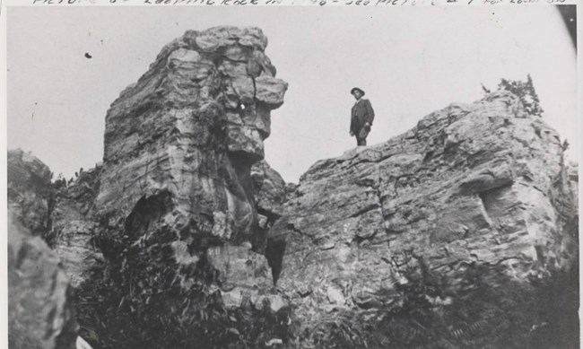 black and white photo of a man standing on a cliff