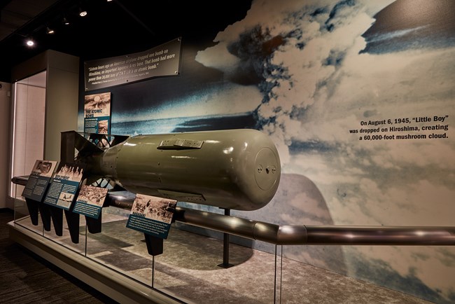 Museum display with a missile against a photo of a mushroom cloud with labels with text in the foreground.