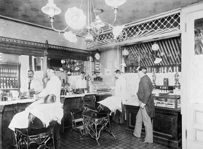 Black and white photo of a man getting his hair cut in a barber shop