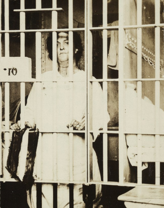 Black and white image of woman behind bars.