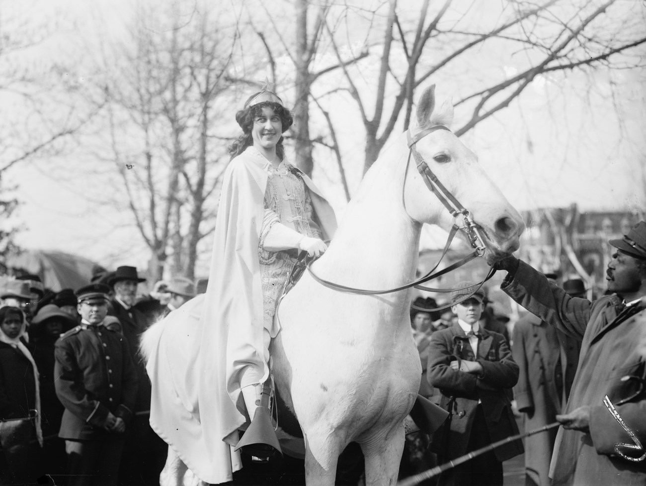 White woman wearing a cape riding a white horse