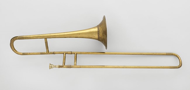 A brass trombone rests on a white surface.