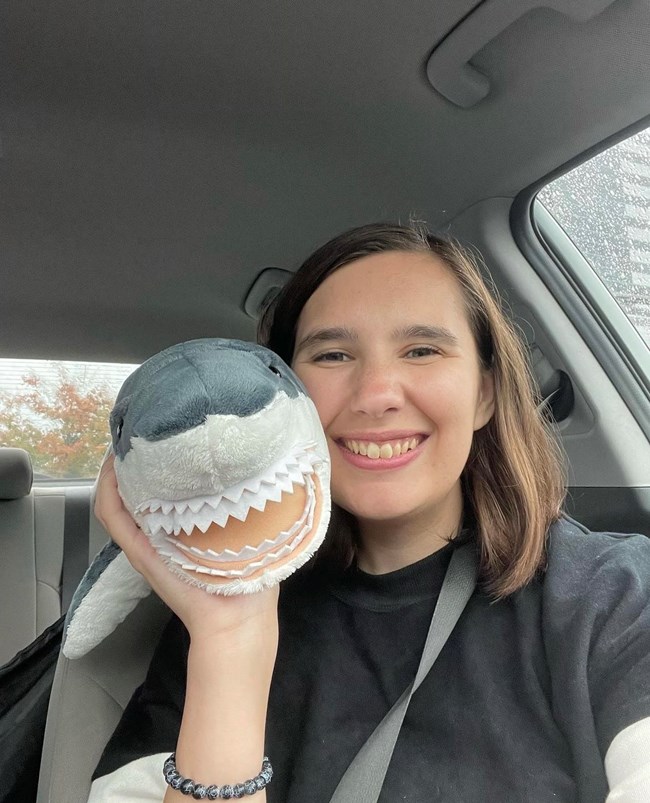 A woman smiles and holds a stuffed shark plush