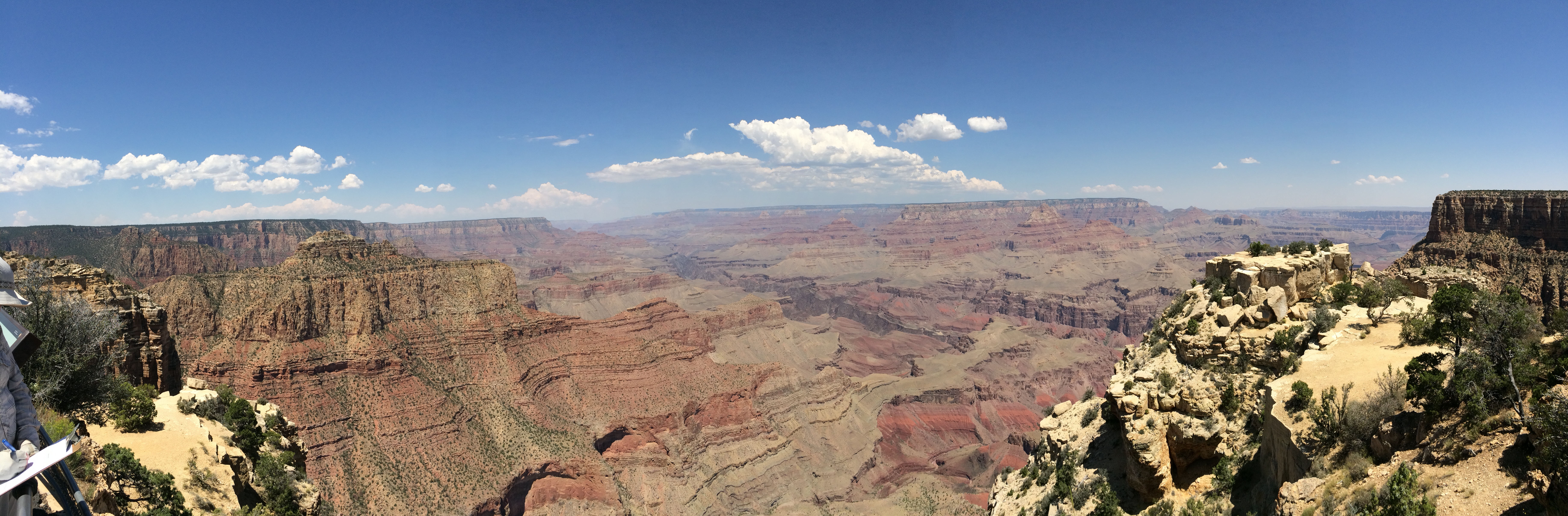 A wide open expanse of a desert canyon with steep, vermilion colored cliffs on both sides and a muddy river within a gorge down below.