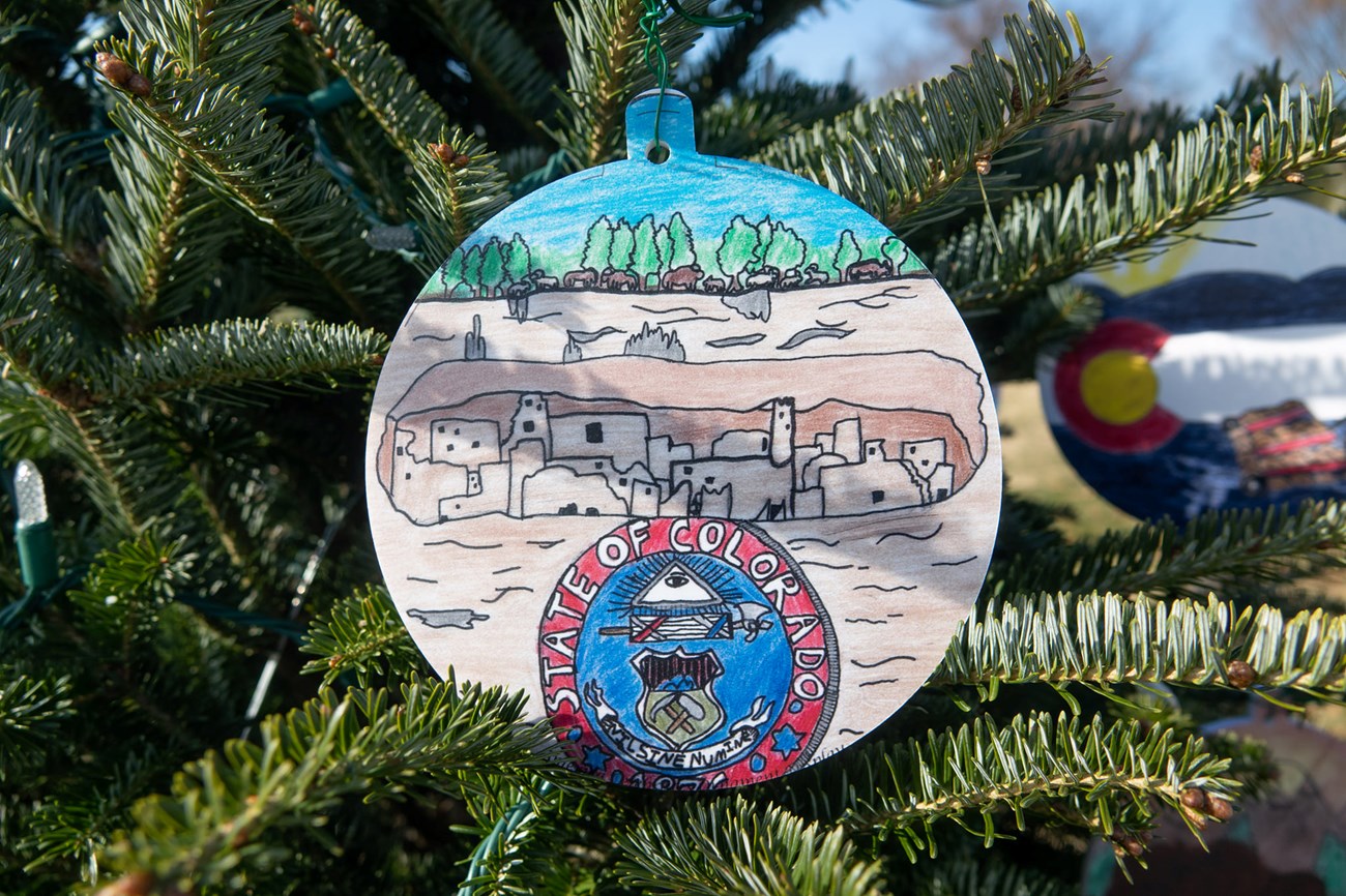 ornament of a drawing of mesa verde's archeological site. The ornament is hanging from christmas tree