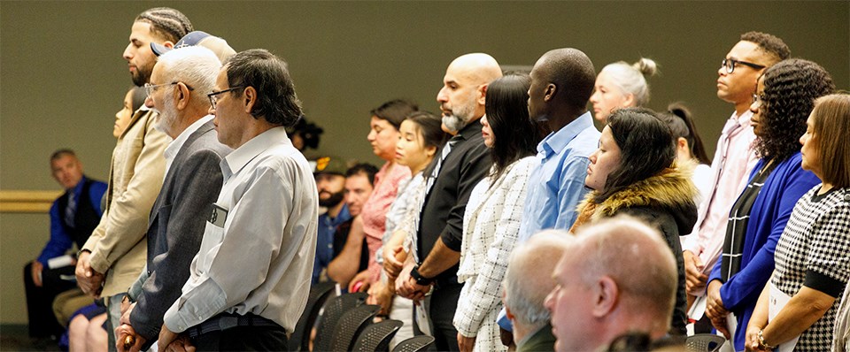 A group of men and women of many nationalities stand facing the front of a room.