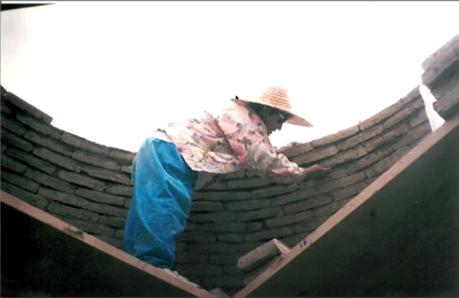 Woman working on an curved adobe wall.