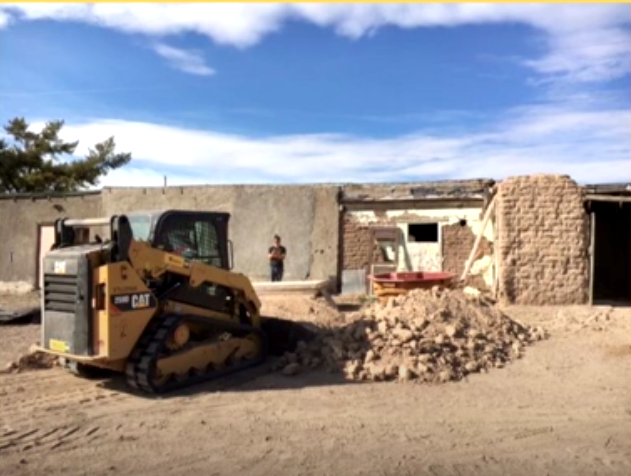 A small bulldozer sits beside a pile of demolished remnants of an adobe building.