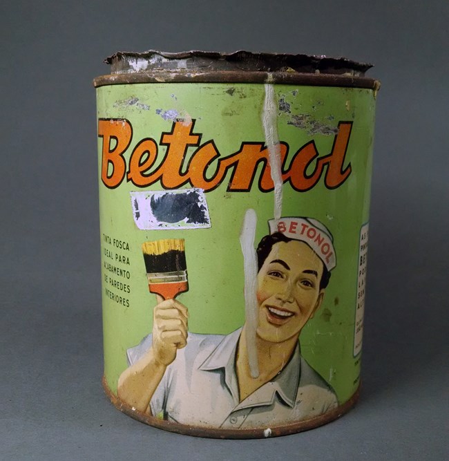 An old green paint can with a cartoon figure holding a paintbrush.