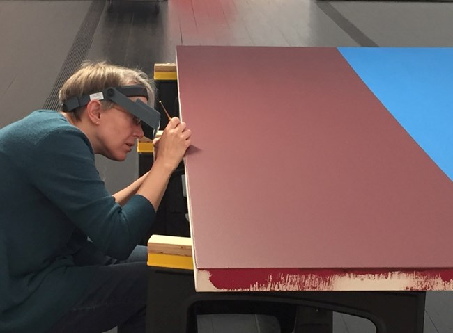 Paint sample being taken from a red colored plywood art piece.