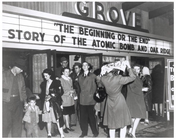 A group of people in front of a movie theater. A man in an usher uniform is in center.