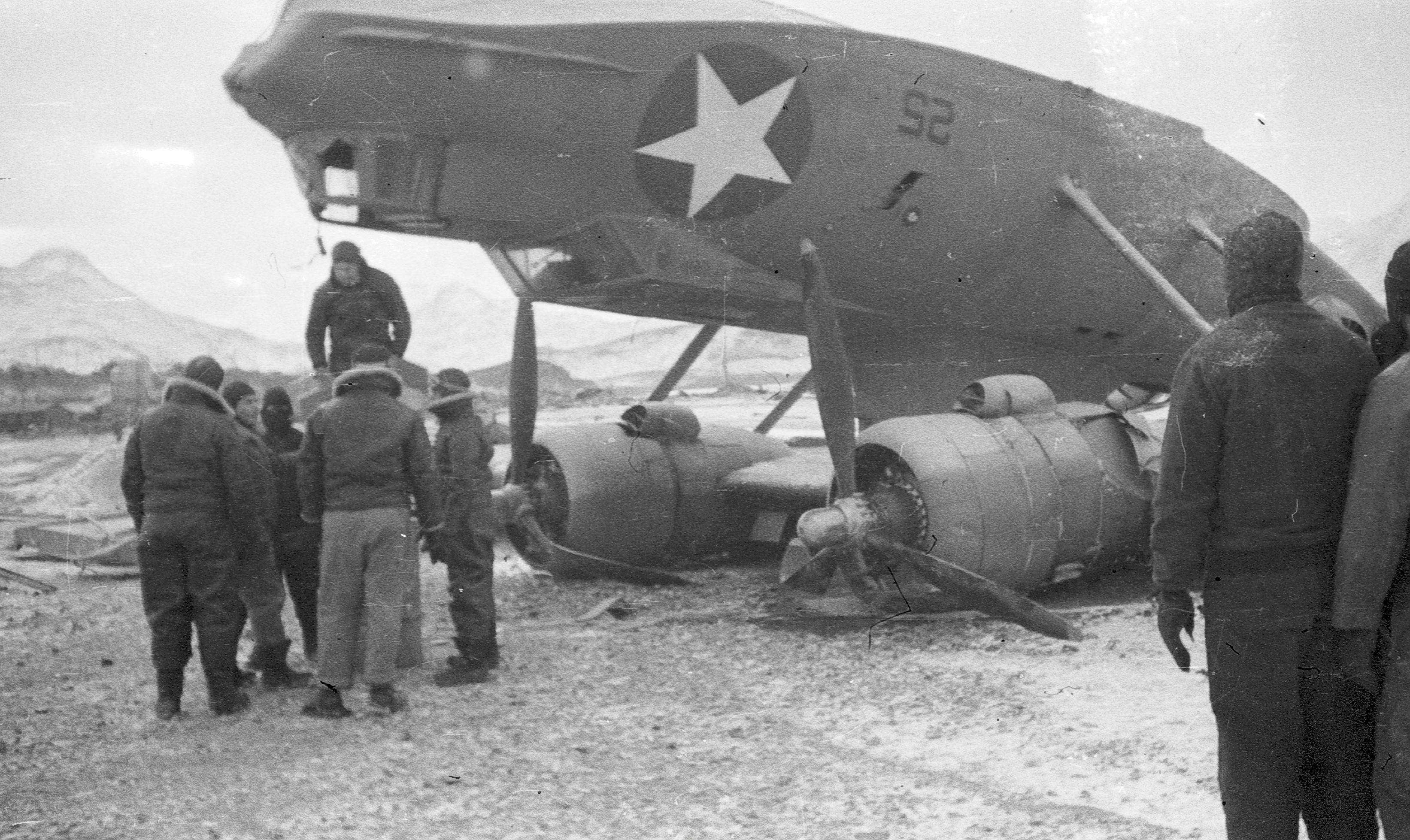 About 10 men standing around an overturned plane.