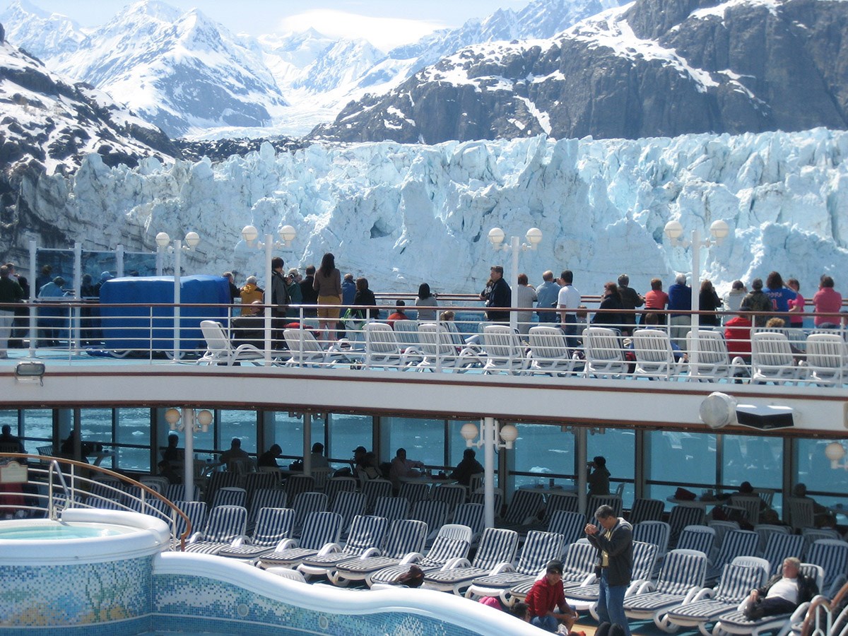 Passengers on a cruise ship line up at the railing to see a glacier up close.