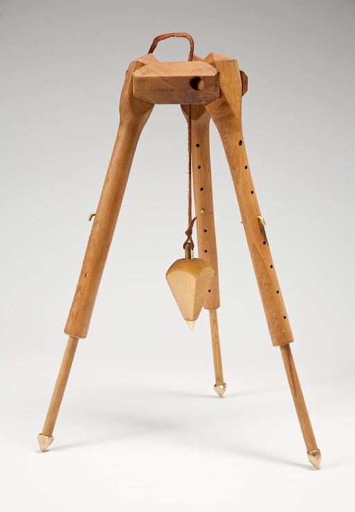 three wooden legs going down from a base, like a stool. Hanging under it is a 3-d triangle held by a rope